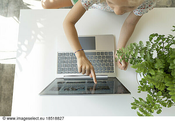 Girl touching screen of laptop on table at home