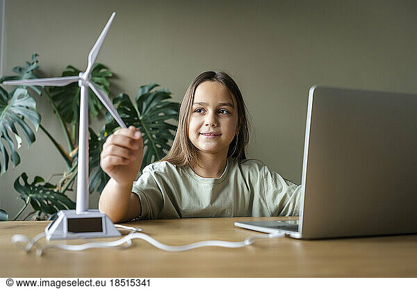 Girl touching wind turbine model on table at home