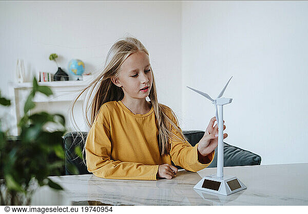 Girl touching wind turbine model on table at home