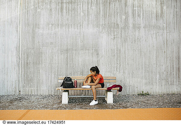 Girl tying shoelace against wall at sports court