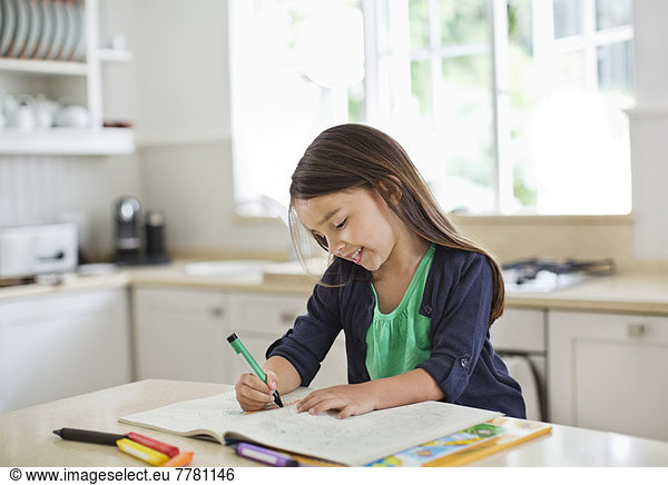 Girl using coloring book in kitchen