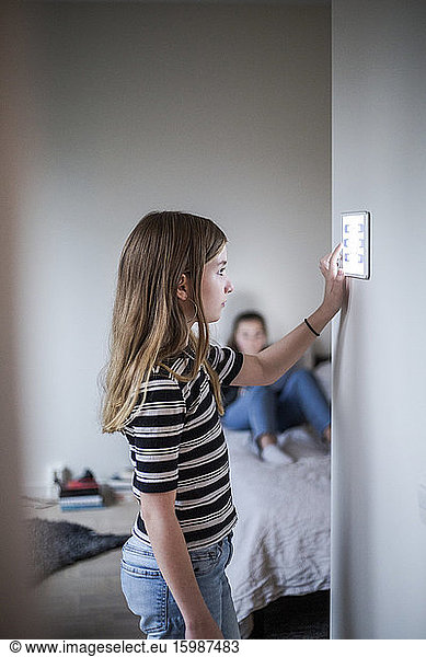 Girl using digital tablet on wall with sister in background at smart home
