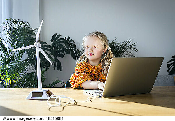 Girl using laptop looking at wind turbine model in green home