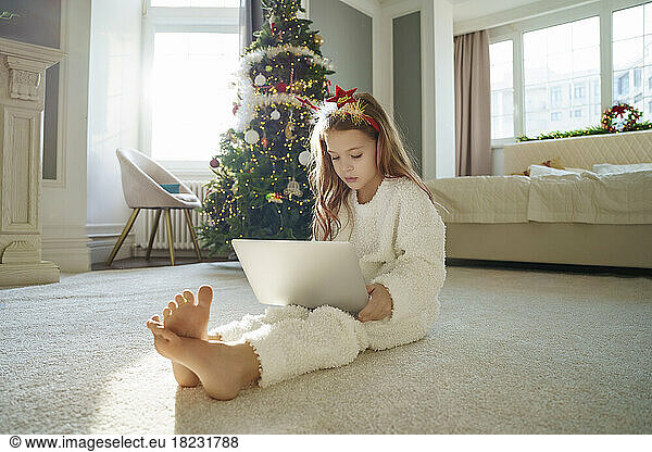 Girl using laptop sitting on carpet in bedroom at home