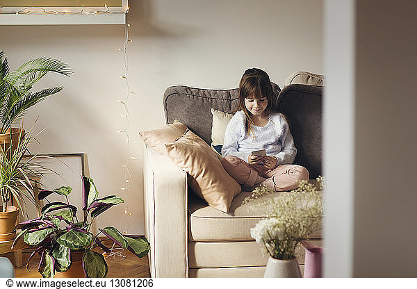 Girl using phone while sitting on sofa at home