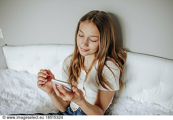 Girl using smart phone sitting on bed at home