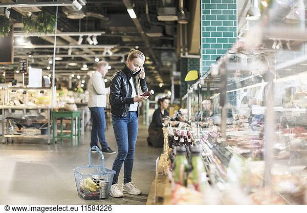 Girl using smart phone while reading label on bottle in organic groceries store