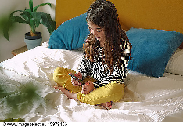 Girl using smartphone sitting on bed