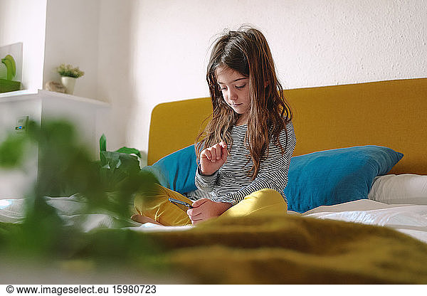 Girl using smartphone sitting on bed