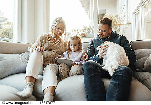 Girl using tablet PC sitting by parents and dog at home