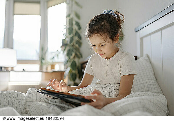 Girl using tablet PC sitting in bedroom