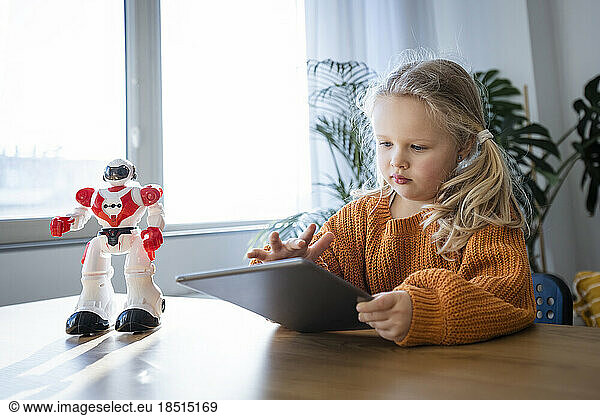 Girl using tablet PC with robot on table at home