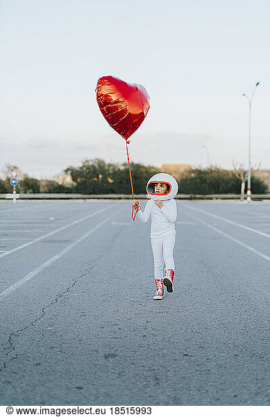 Girl walking in parking lot with red heart shape balloon