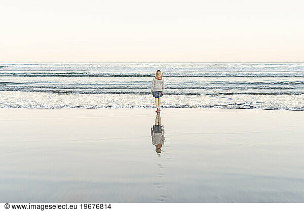 Girl walking on beach with serene reflection