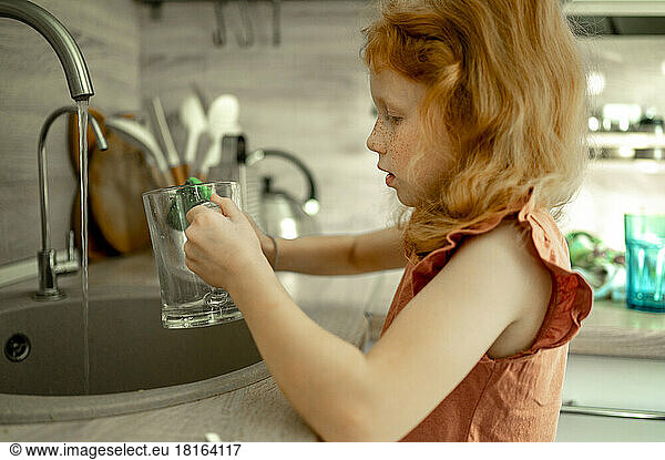 Girl washing glass in kitchen