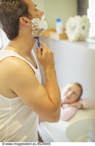 Girl watching father shave in bathroom