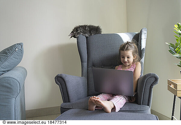 Girl watching laptop sitting in armchair at home