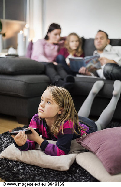 Girl watching TV on floor with family in background
