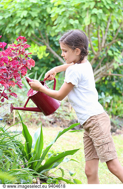 Girl watering plants in garden with red watering can