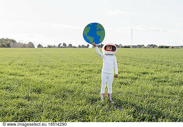 Girl wearing astronaut costume holding cut out of earth standing on grass