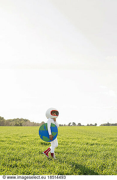 Girl wearing astronaut costume holding earth cut out standing on grass