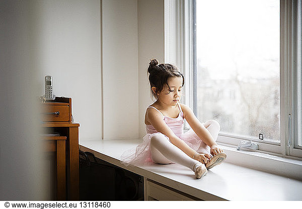 Girl wearing ballet shoes while sitting on table by window at home