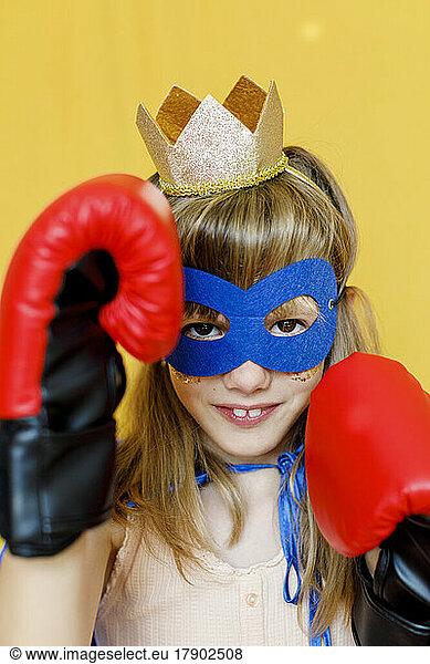 Girl wearing boxing gloves and mask against yellow background