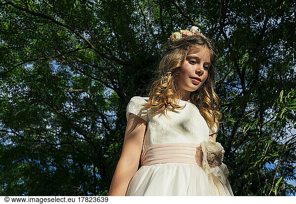Girl wearing communion dress standing under tree