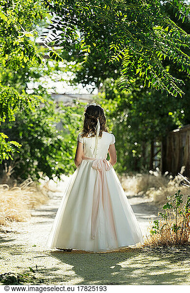 Girl wearing communion dress walking on footpath in forest