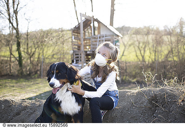 Girl wearing face mask  sitting in garden  playing with her dog