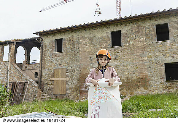 Girl wearing hardhat standing with drawing in front of house