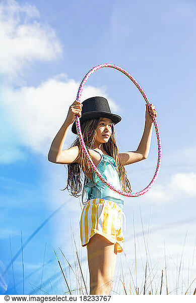 Girl wearing hat holding plastic hoop under sky