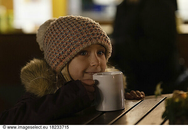 Girl wearing knit hat drinking tea in Christmas market at night