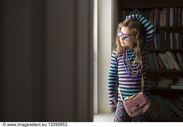 Girl wearing necklace and sunglasses standing by window at home