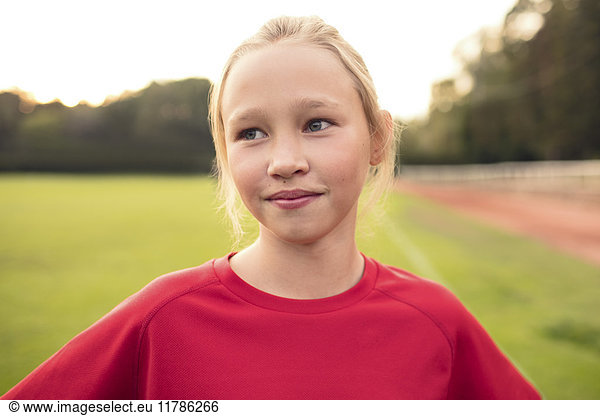 Girl wearing red t-shirt standing on soccer field against sky
