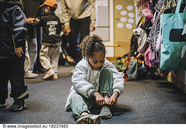Girl wearing shoe while sitting on carpet at day care center