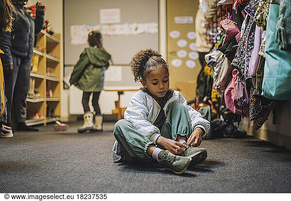 Girl wearing shoe while sitting on carpet in kindergarten
