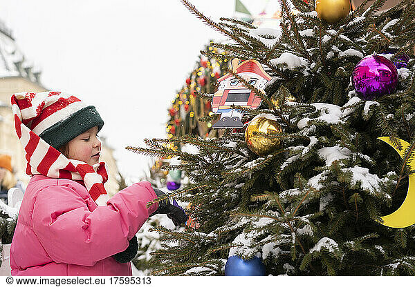 Girl wearing striped knit hat touching Christmas tree