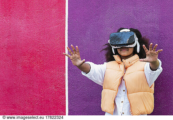 Girl wearing virtual reality simulator gesturing in front of purple and pink wall