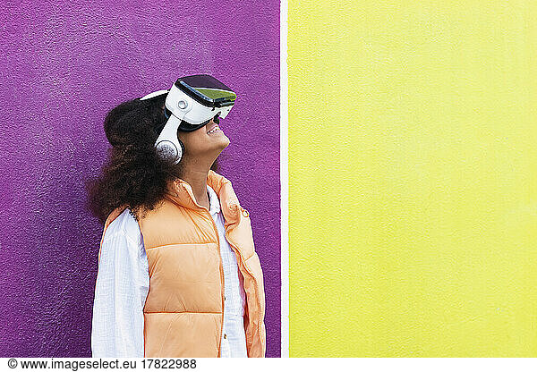 Girl wearing virtual reality simulator standing in front of yellow and purple wall