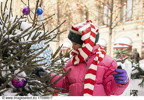 Girl wearing warm clothing touching Christmas tree at market