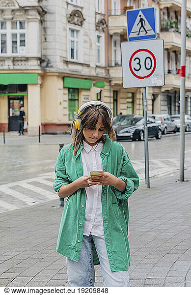 Girl wearing wireless headphones using smart phone at footpath