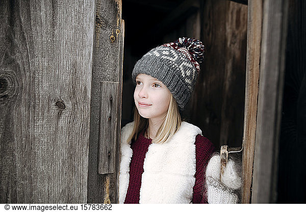 Girl wearing woolly hat at wooden door