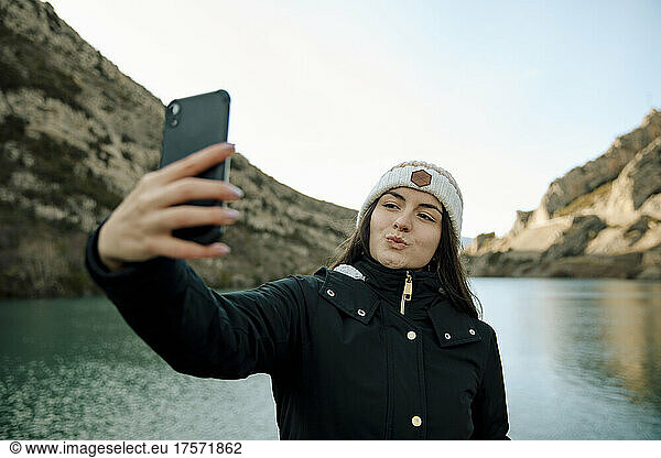 Girl with a wool hat taking a selfie with her cell phone on a pier