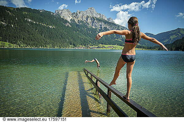 Girl with arms outstretched balancing on railing amidst lake