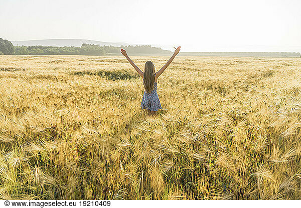 Girl with arms outstretched standing amidst crop in wheat field