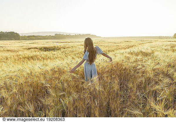 Girl with arms outstretched standing amidst wheat crop in field