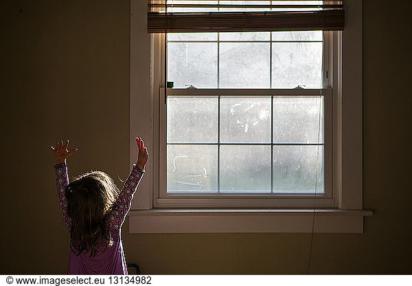 Girl with arms raised standing by window at home