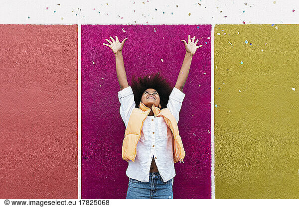 Girl with arms raised throwing confetti standing in front of colorful wall