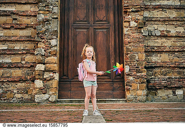 Girl with backpack and paper windmill looking at camera